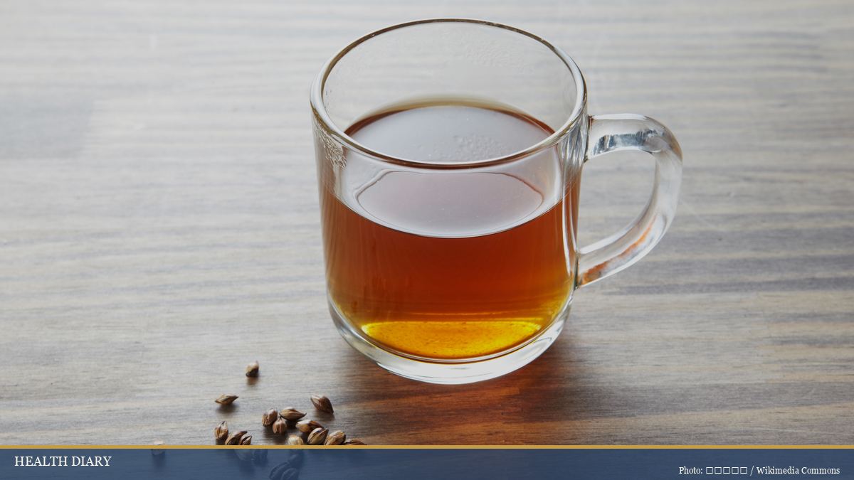 Glass mug of warm Korean boricha barley tea beside roasted barley grains on a table