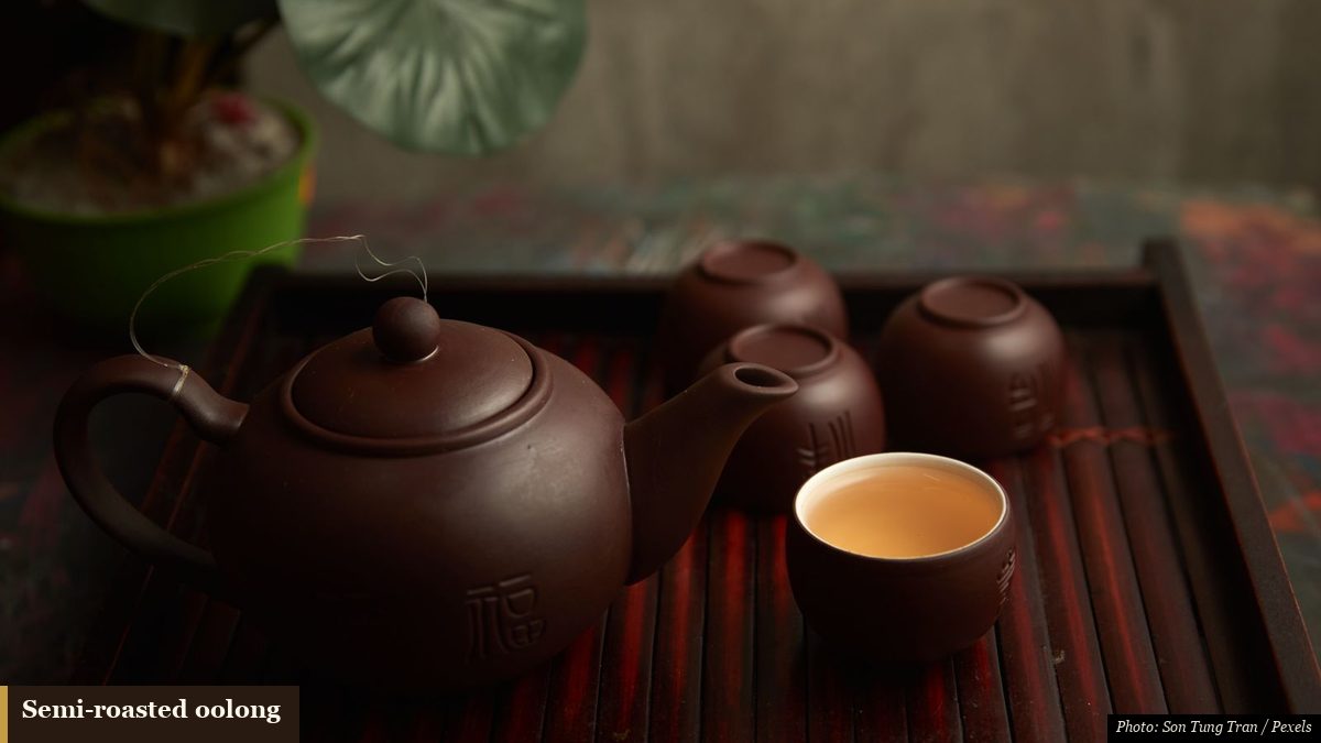 Amber oolong tea in a cup beside a purple-clay Yixing teapot on a mat