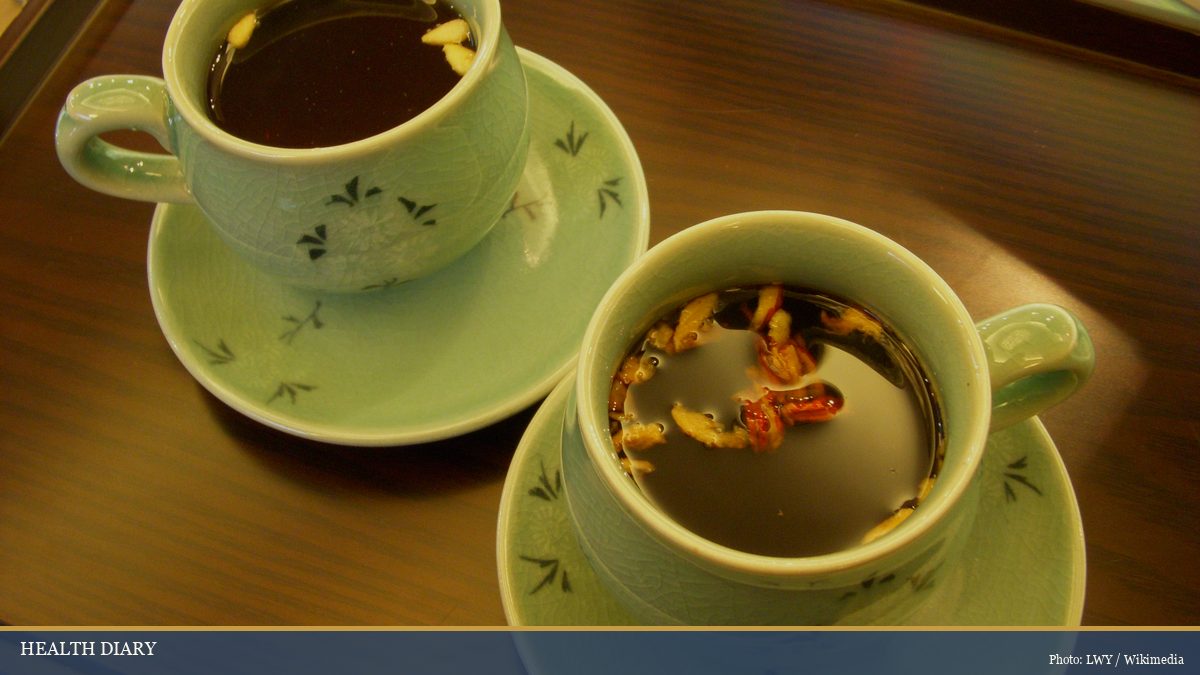 Two celadon Korean teacups holding warm jujube tea on a wooden tray