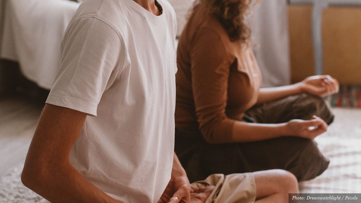 Two people sitting quietly in seated breathing meditation together at home