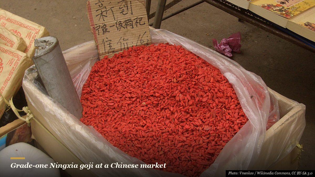 Bright red dried Ningxia goji berries for sale in a Chinese market with a handwritten sign