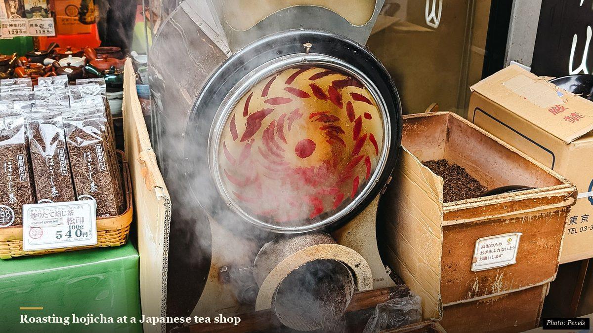 Traditional hojicha roaster steaming at a Japanese tea shopfront beside bags of roasted tea