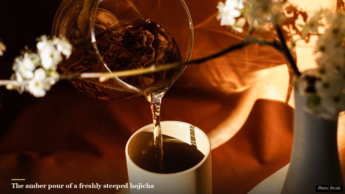 Amber hojicha tea being poured from a Japanese kyusu teapot into a cup