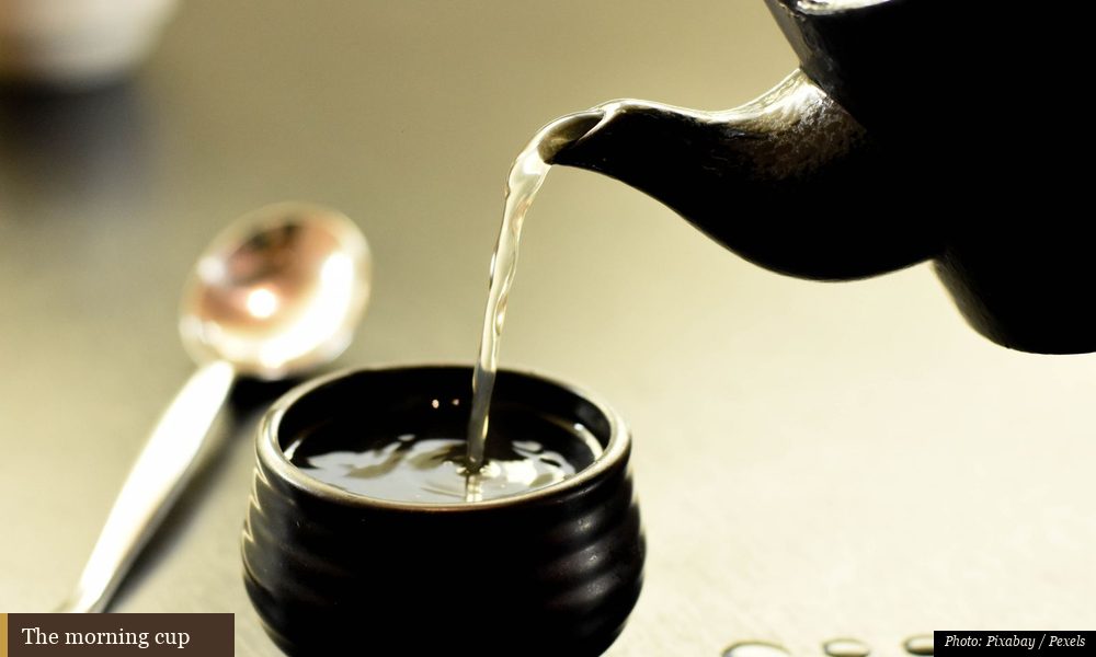 Person pouring hot morning tea into a small cup by a sunlit window