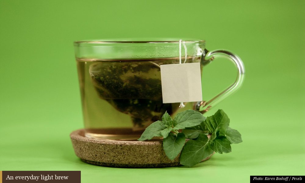 Clear glass cup of light herbal tea with fresh mint on a cork coaster