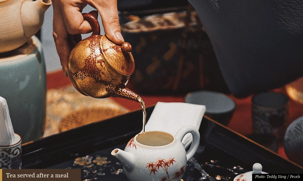 Small clay teapot and cups served after a family meal on a wooden table