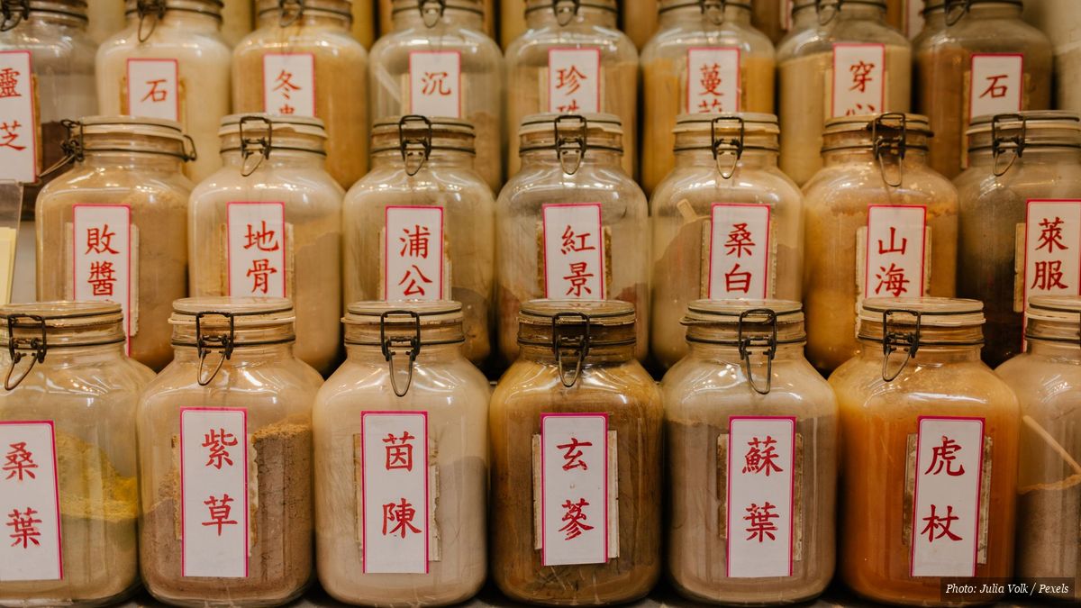 Glass jars of herbal powders with Chinese labels lined up in a traditional pharmacy