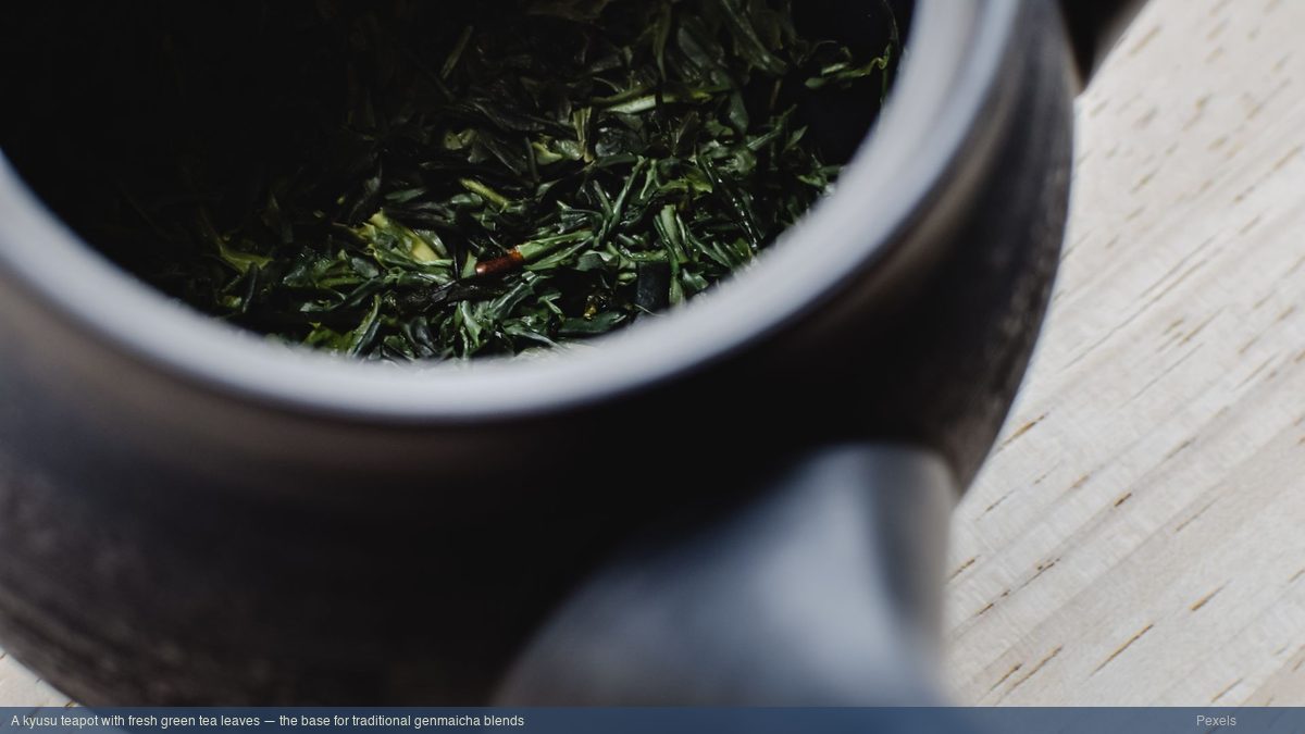 A Japanese kyusu teapot with fresh green tea leaves inside, ready for brewing on a wooden surface