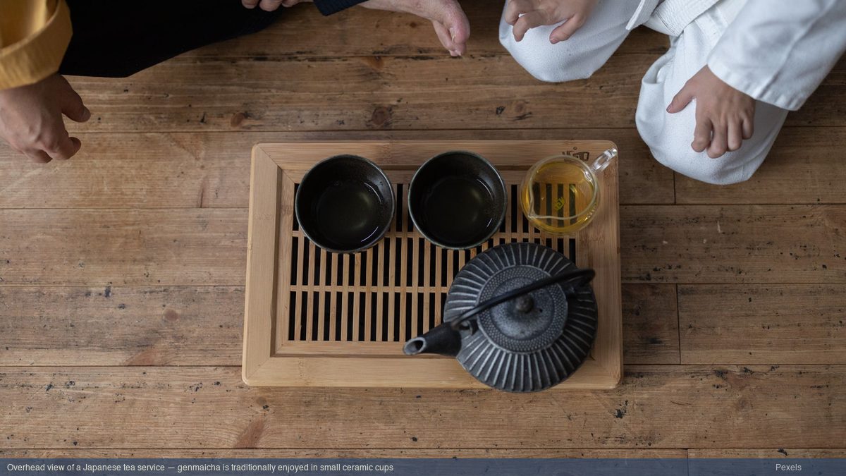 Overhead view of a Japanese tea service with iron teapot and ceramic cups on a bamboo tray
