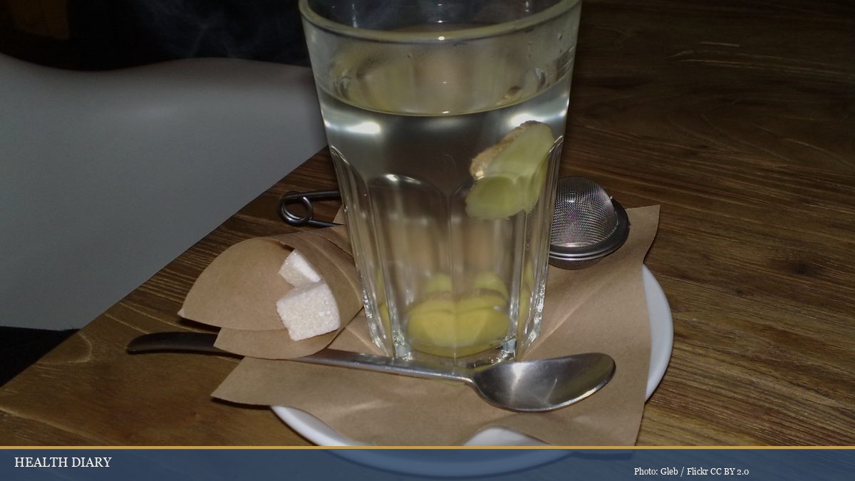 Glass of steeping ginger tea with fresh ginger slices and rock sugar cubes on wooden tray