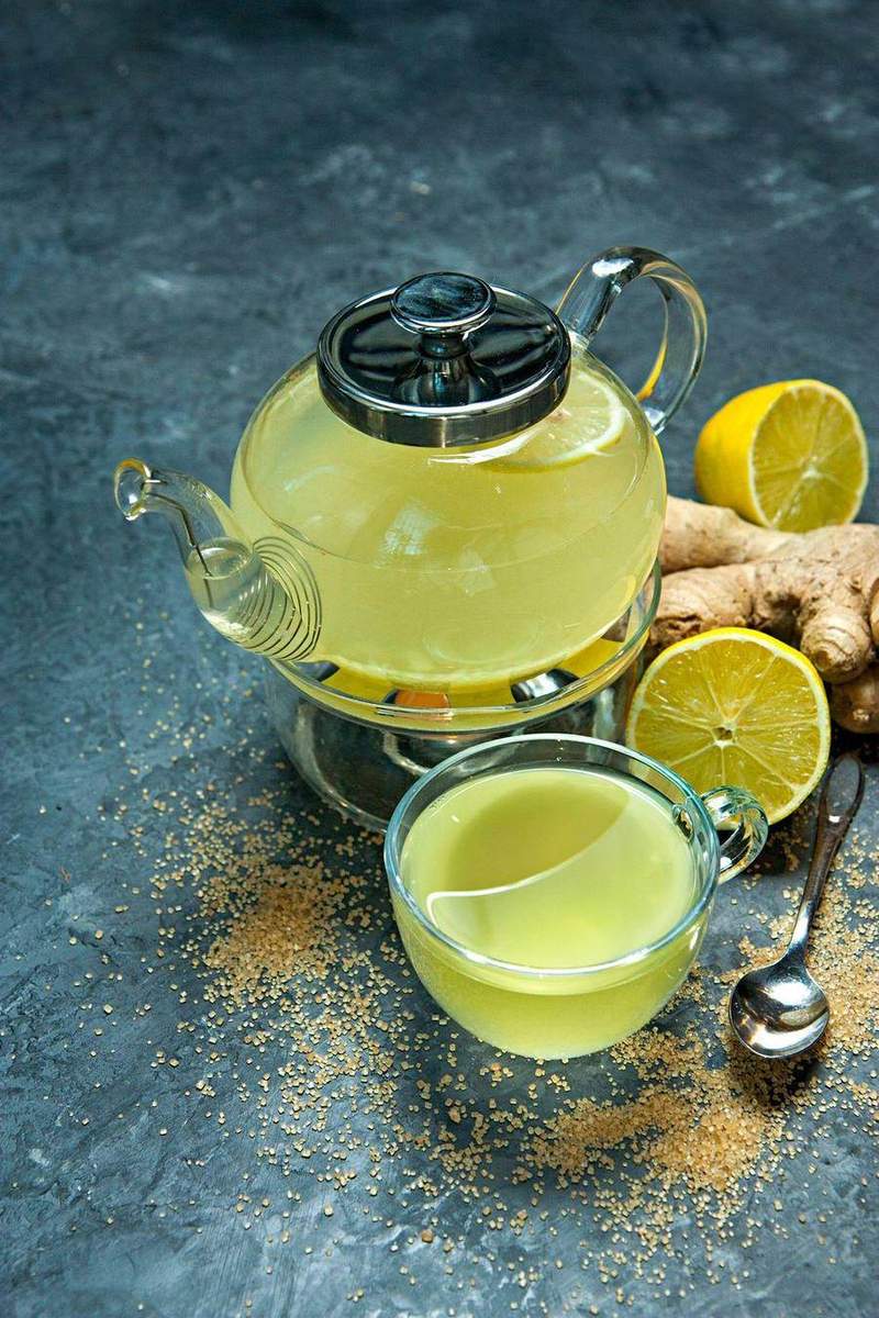 Glass teapot and cup of freshly brewed ginger lemon tea with raw ginger root