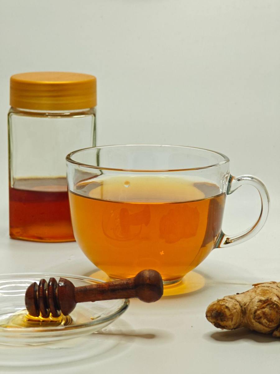 Warm ginger honey tea in glass cup with honey jar and ginger root