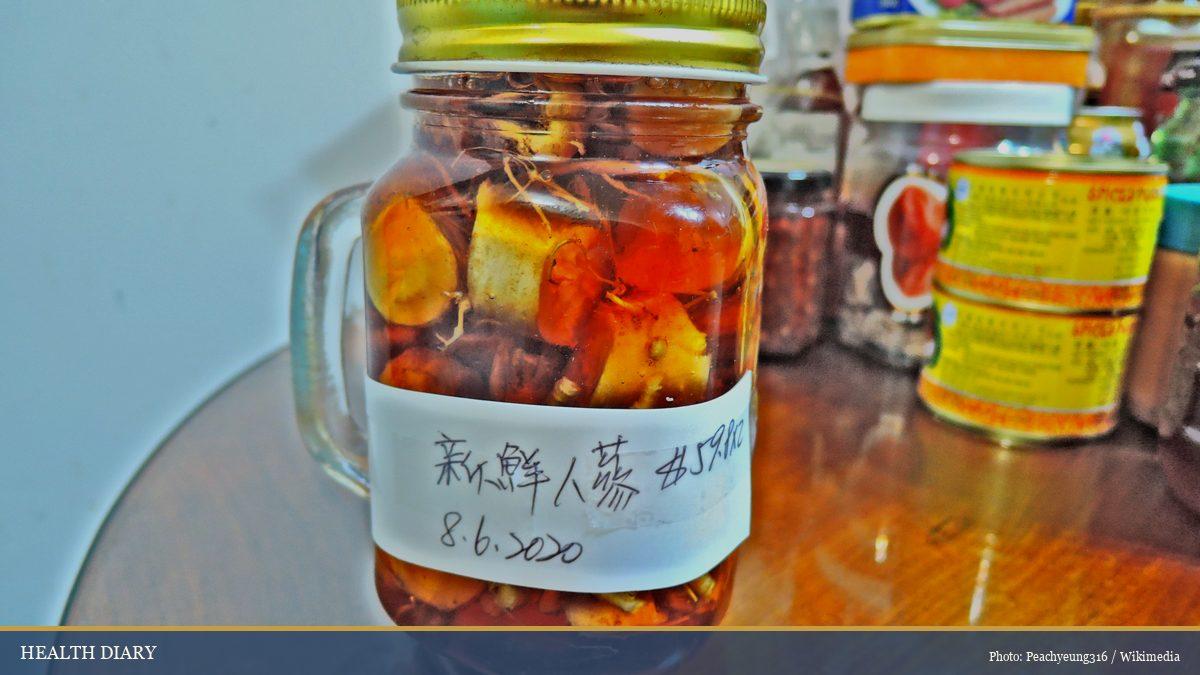 Sliced fresh ginseng root preserved in honey inside a labeled glass jar, a traditional home preparation
