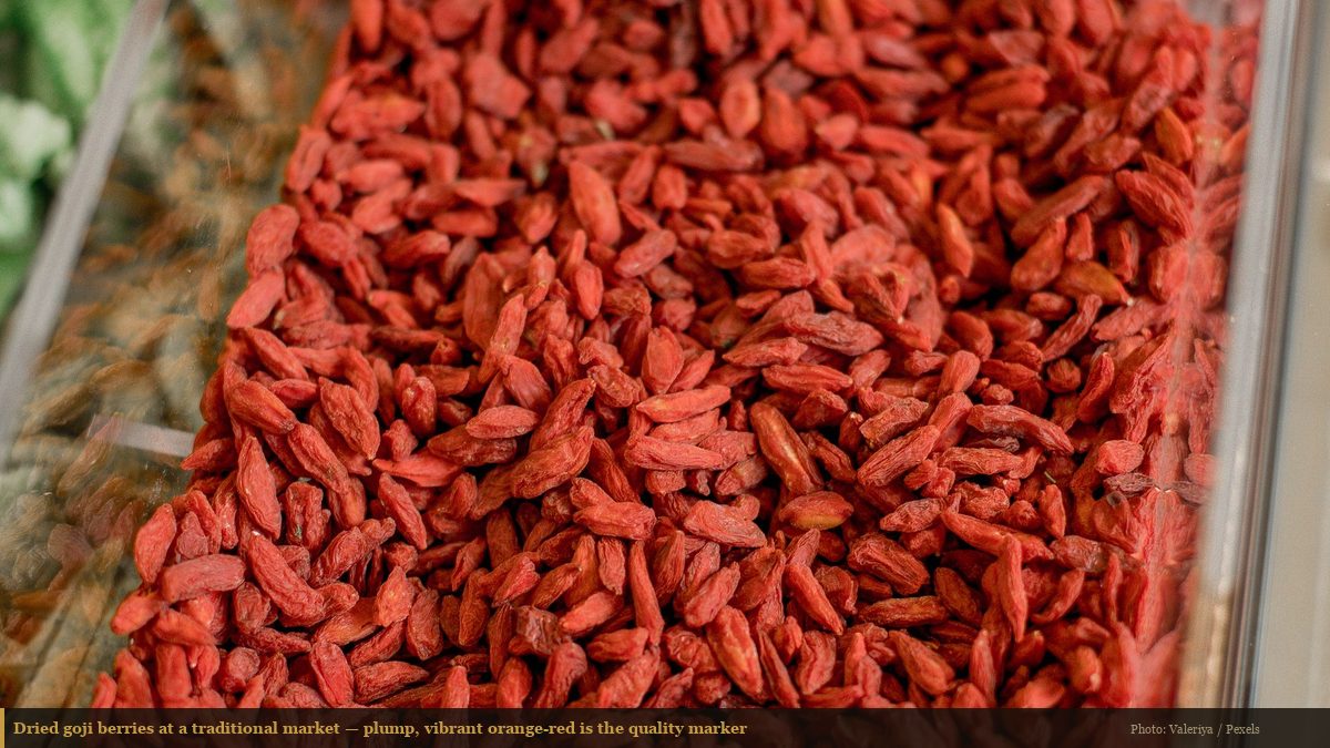 Dried goji berries displayed in a clear market container showing vibrant orange-red color and plump texture