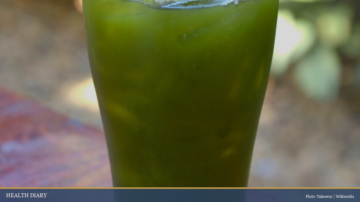 Tall glass of vivid green nuoc rau ma gotu kola juice with ice, served outdoors on a wooden table