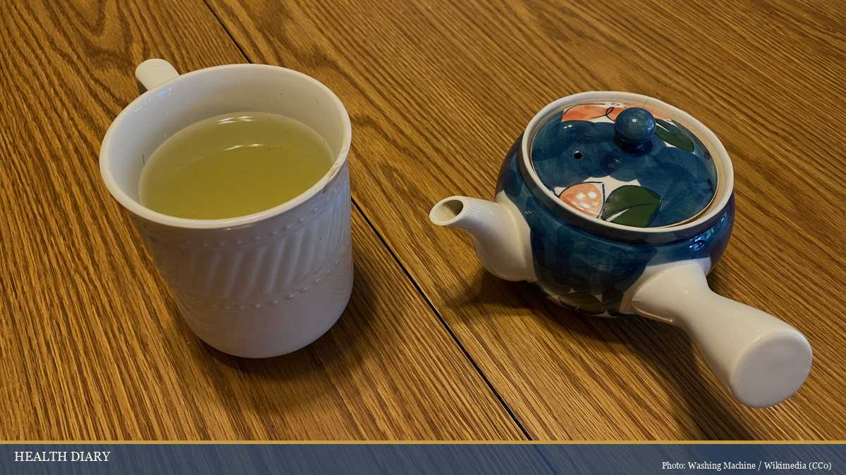 Japanese kyusu teapot beside a porcelain tea cup of brewed green tea on a wooden table for everyday use