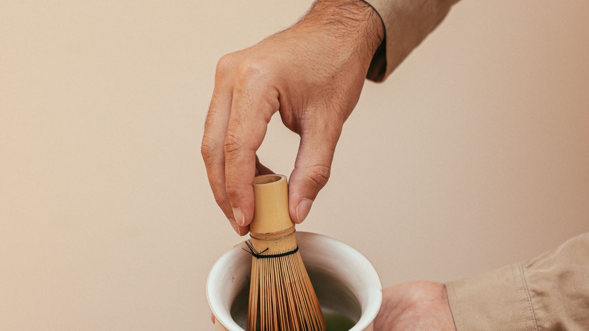 Hands whisking ceremonial matcha in a chawan bowl on a wooden surface