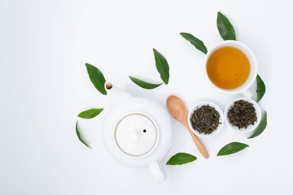 A cup of pale green herbal tea beside a small teapot
