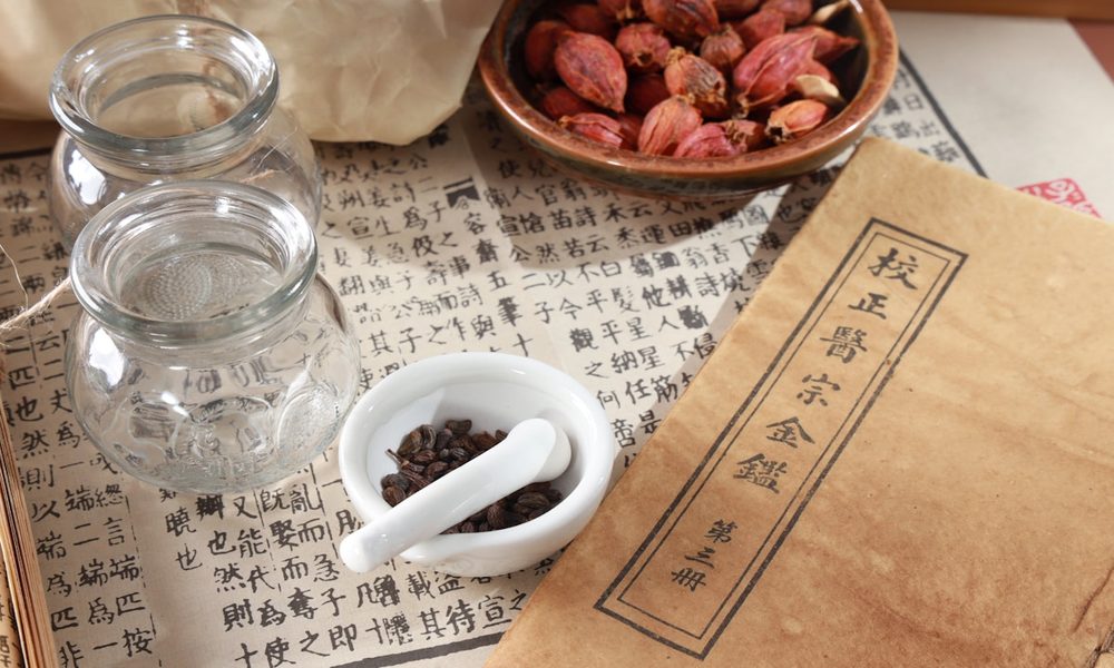 Classical Japanese herbal text with dried herbs and mortar pestle representing Kampo's deep textual tradition