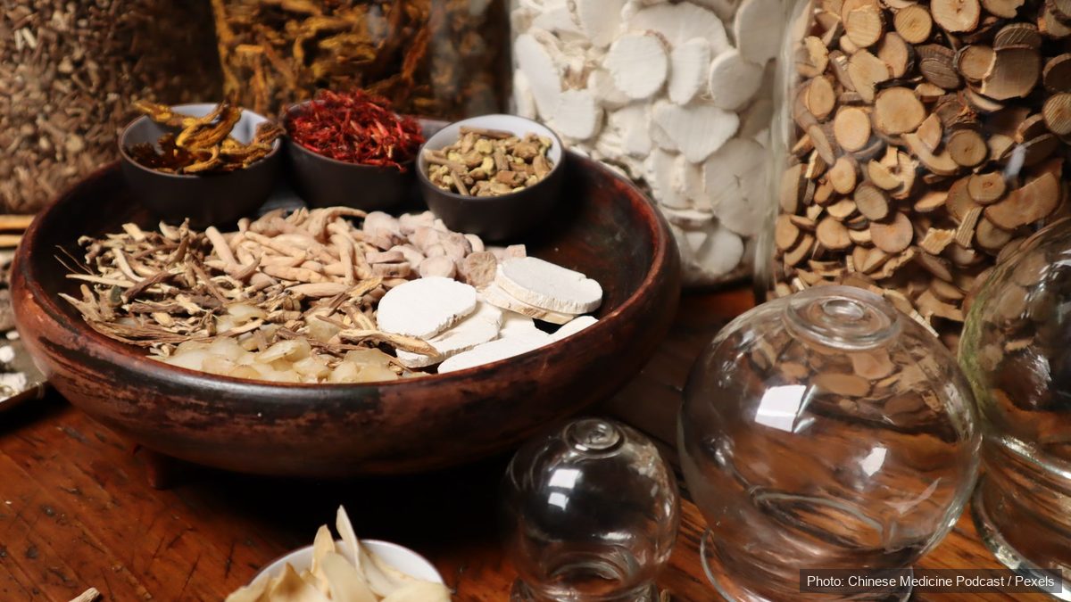 Dried traditional Chinese herbs in bowls beside clear glass cupping jars