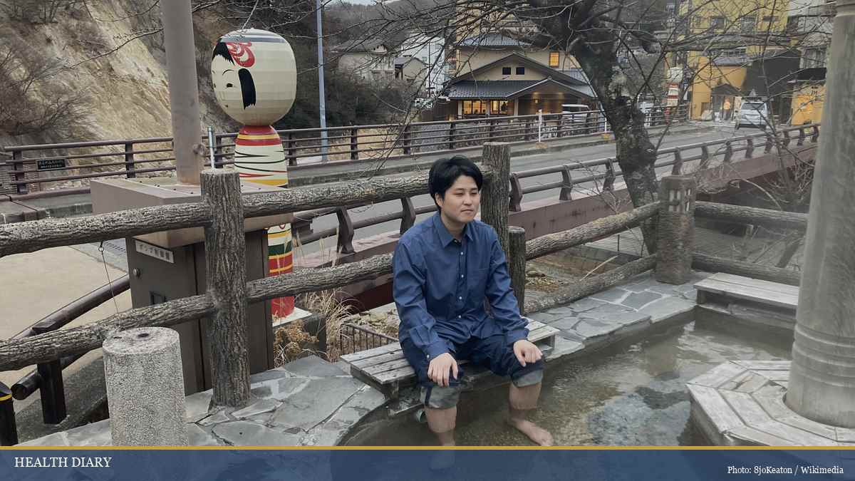 Traveler dipping feet in a traditional Japanese ashiyu street footbath at dusk