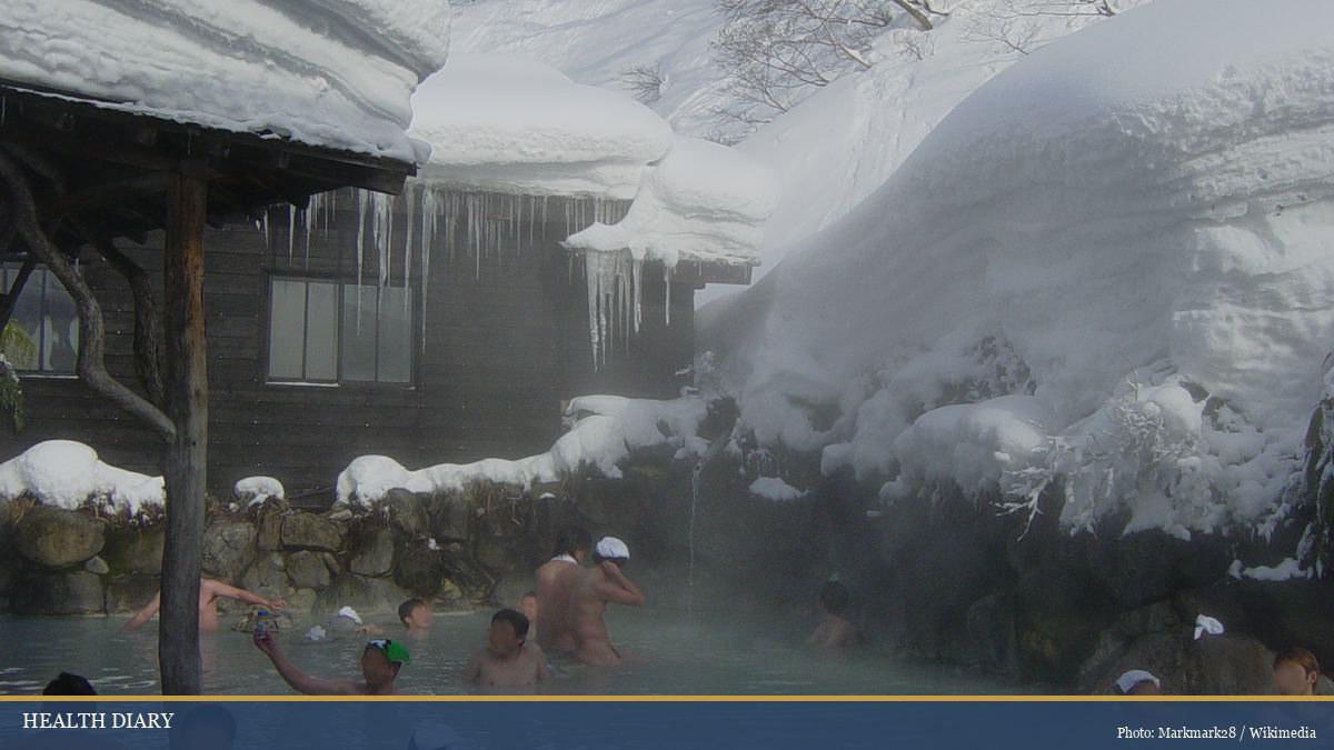 Snow-covered outdoor onsen rotenburo with bathers in a winter Japanese hot spring