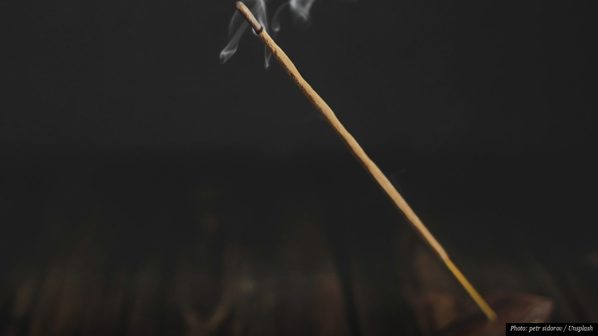 Thin trail of incense smoke curling upward against a dark background