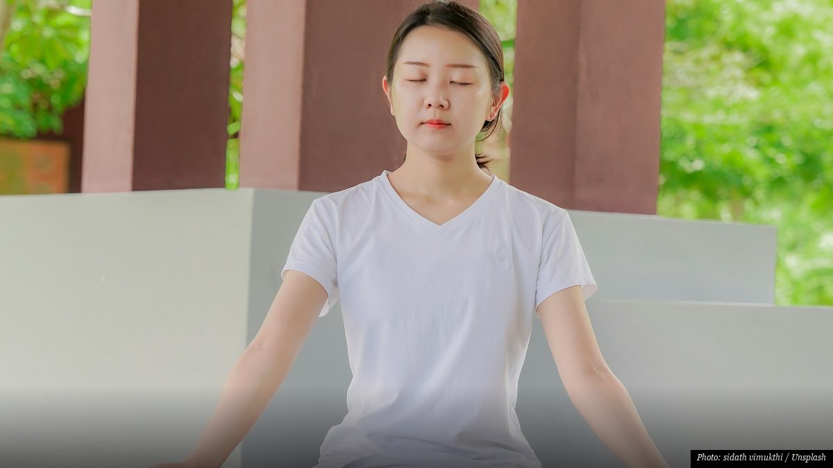 Woman sitting quietly in seated meditation with eyes closed and calm breathing