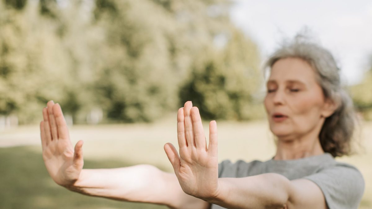 Senior woman practicing a slow qigong pushing movement outdoors in sunlight