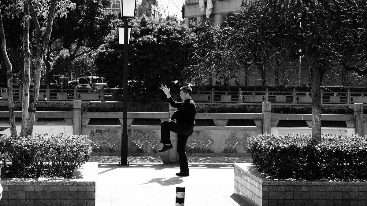 Man balancing on one leg practicing tai chi in a Chinese city park