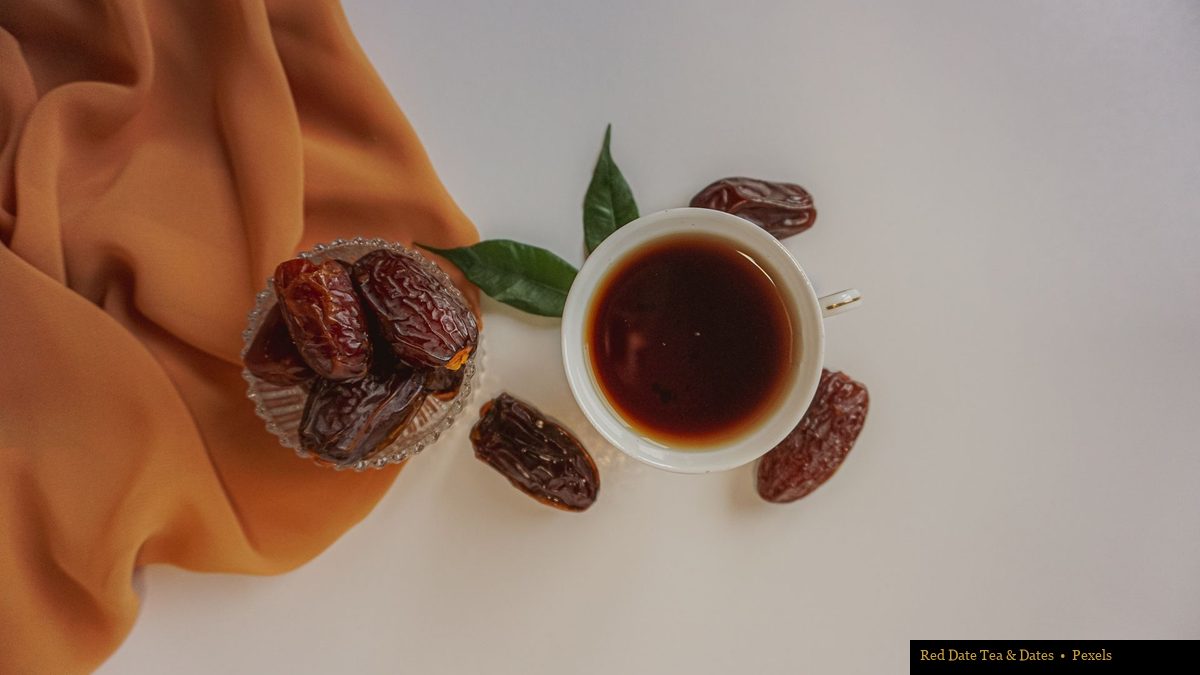 Overhead view of a white tea cup with dark tea surrounded by dates, green leaves, and orange fabric