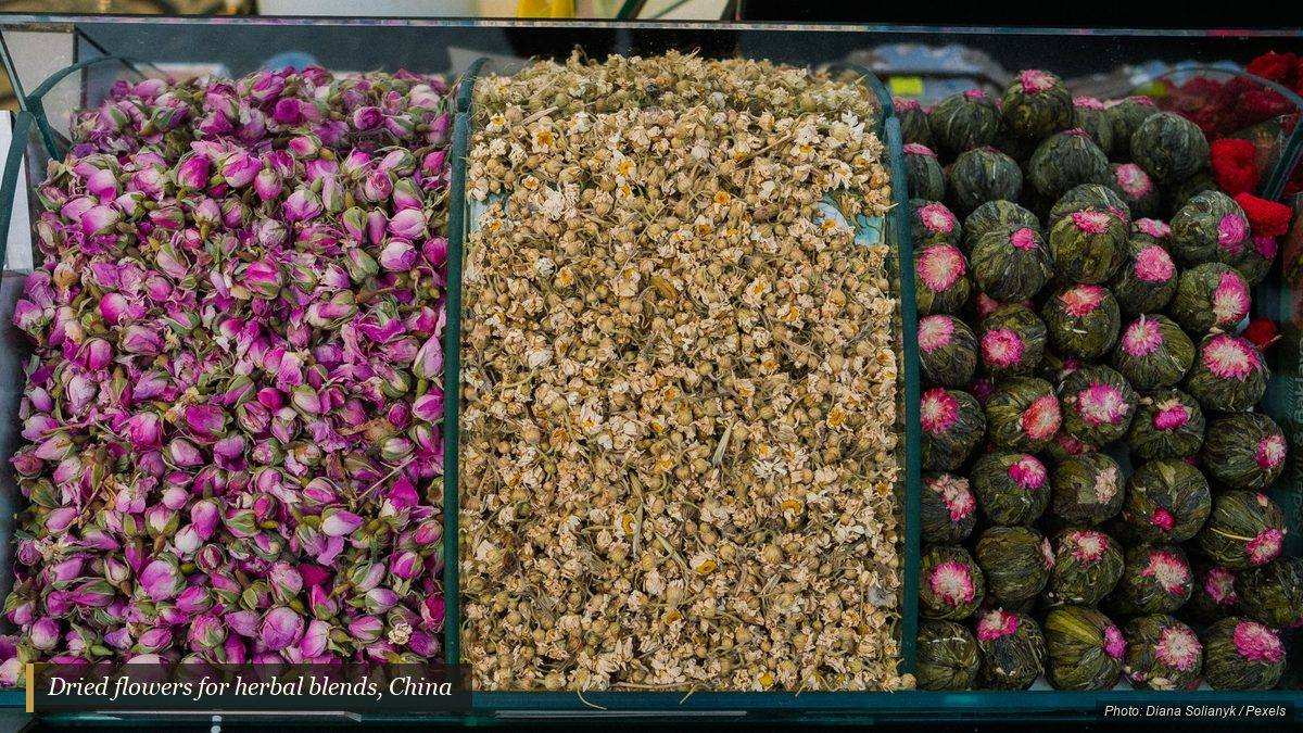 Trays of dried rose buds, chamomile, and flowering tea at a herb market stall
