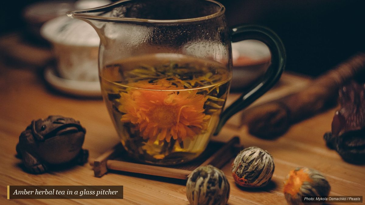 Amber herbal tea steeping in a clear glass pitcher on a wooden table