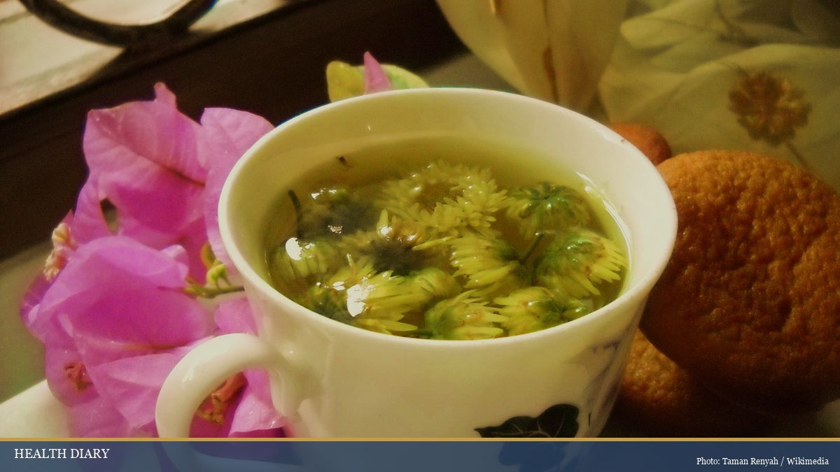 White ceramic cup of warm chrysanthemum tea with whole flowers floating during steeping