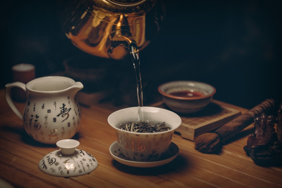 Traditional Japanese kyusu teapot being used to pour bright green sencha tea into a small ceramic cup on a wooden surface