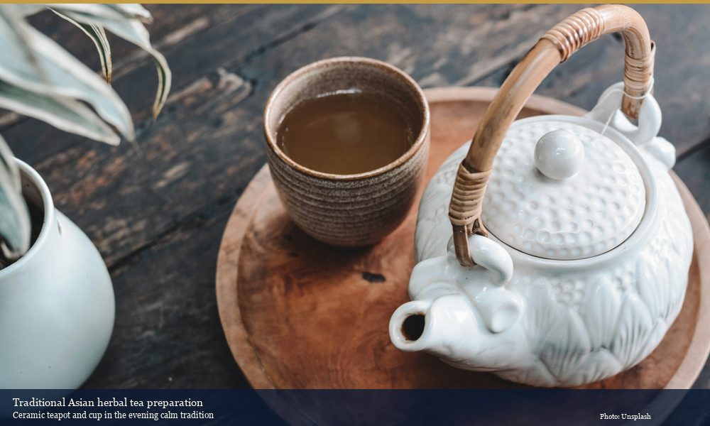 Asian ceramic teapot and tea cup on wooden tray representing traditional herbal tea preparation