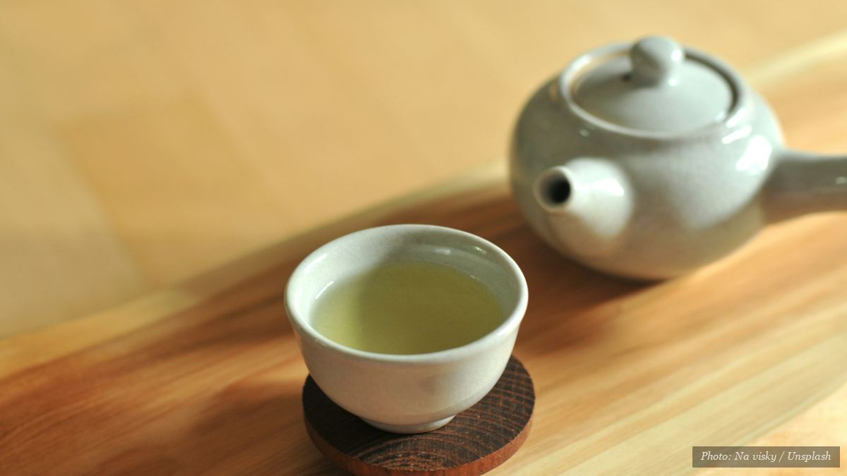 Cup of fresh spring green tea beside a Japanese teapot