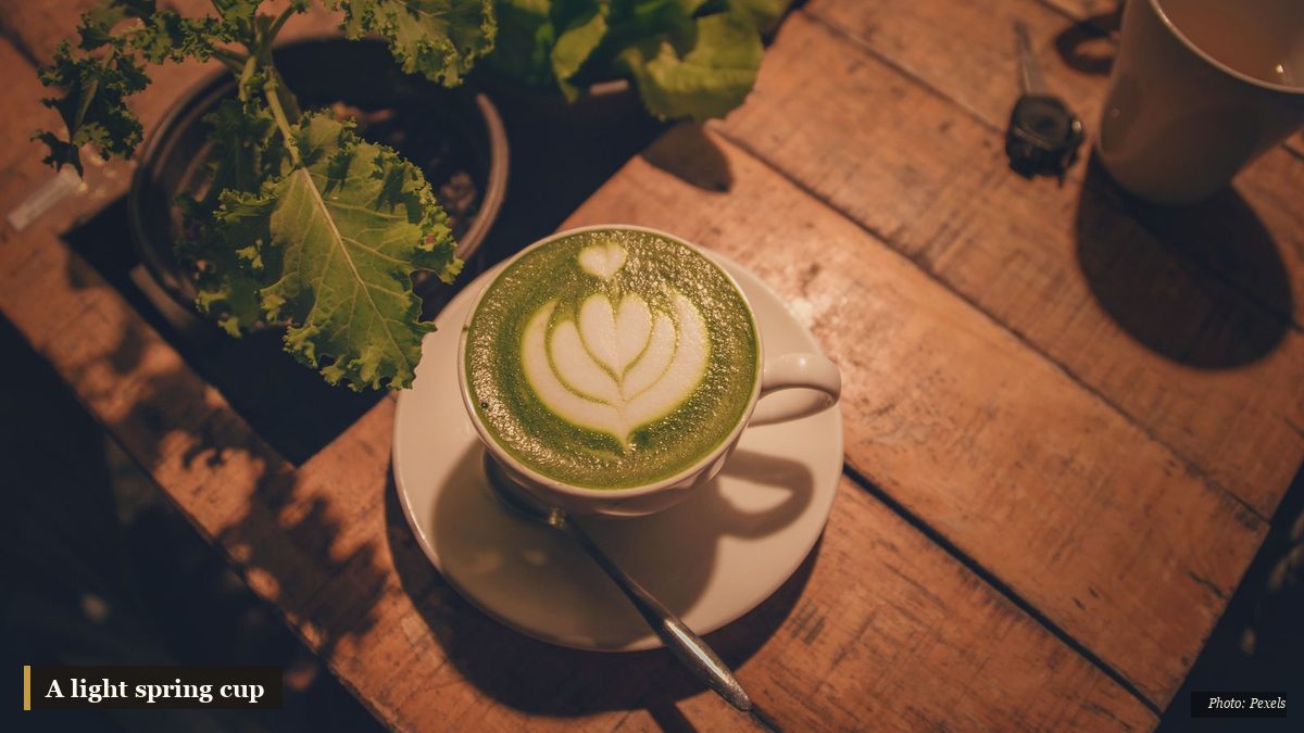 Cup of light green herbal tea on a table beside fresh spring leaves