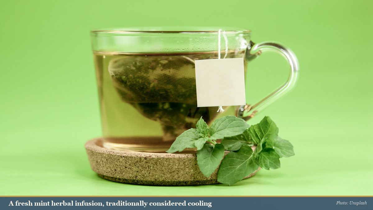 A glass mug of pale mint herbal tea with fresh mint leaves, traditionally considered cooling
