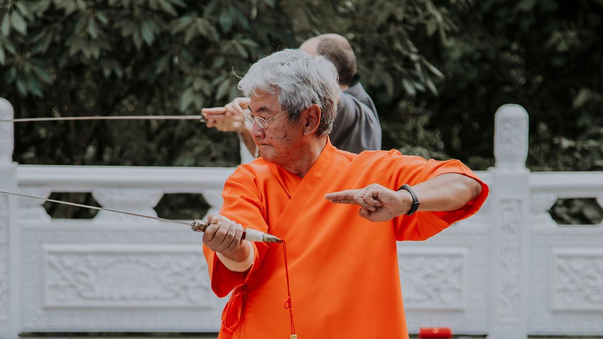 Older practitioner performing a tai chi sword routine in a courtyard