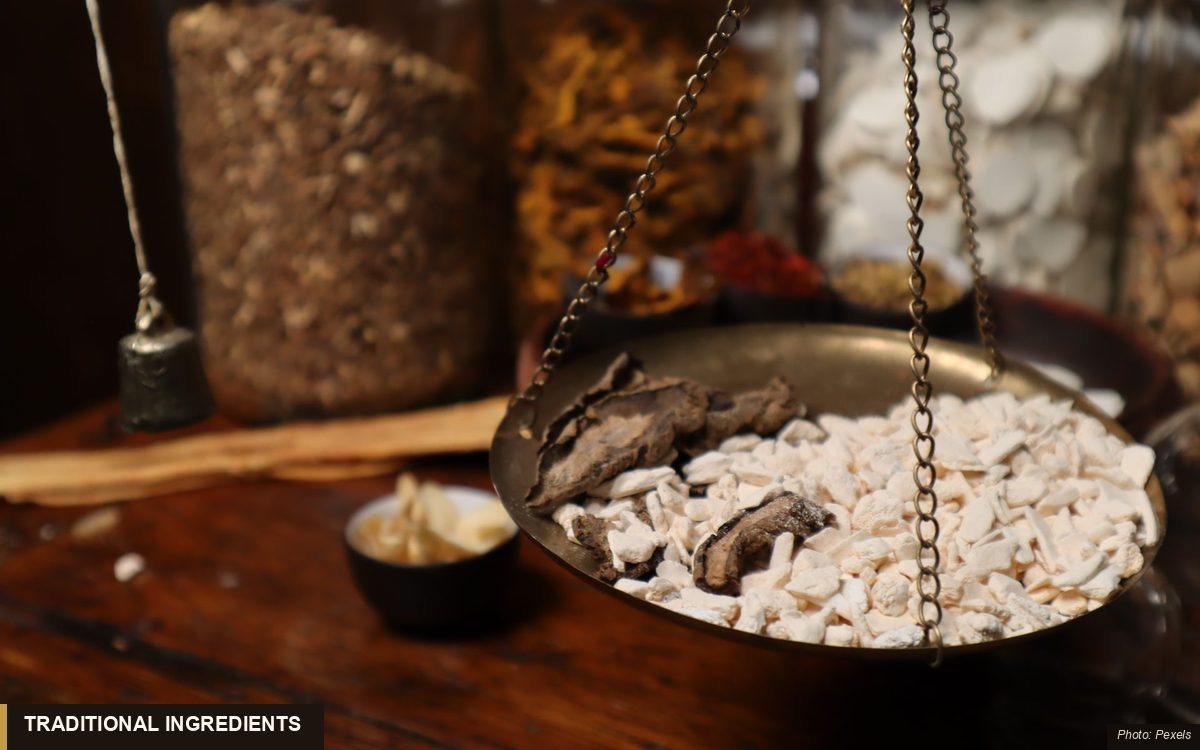 Dried Chinese herbs and sliced roots weighed on a brass apothecary scale