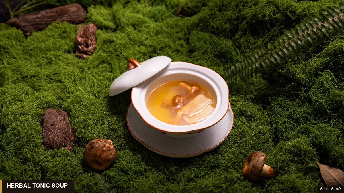Lidded ceramic bowl of Asian herbal tonic soup with mushrooms and roots