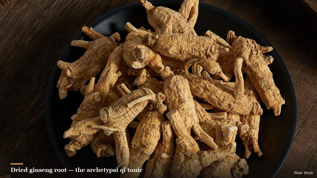 Dried ginseng roots piled in a dark ceramic bowl on a wooden table