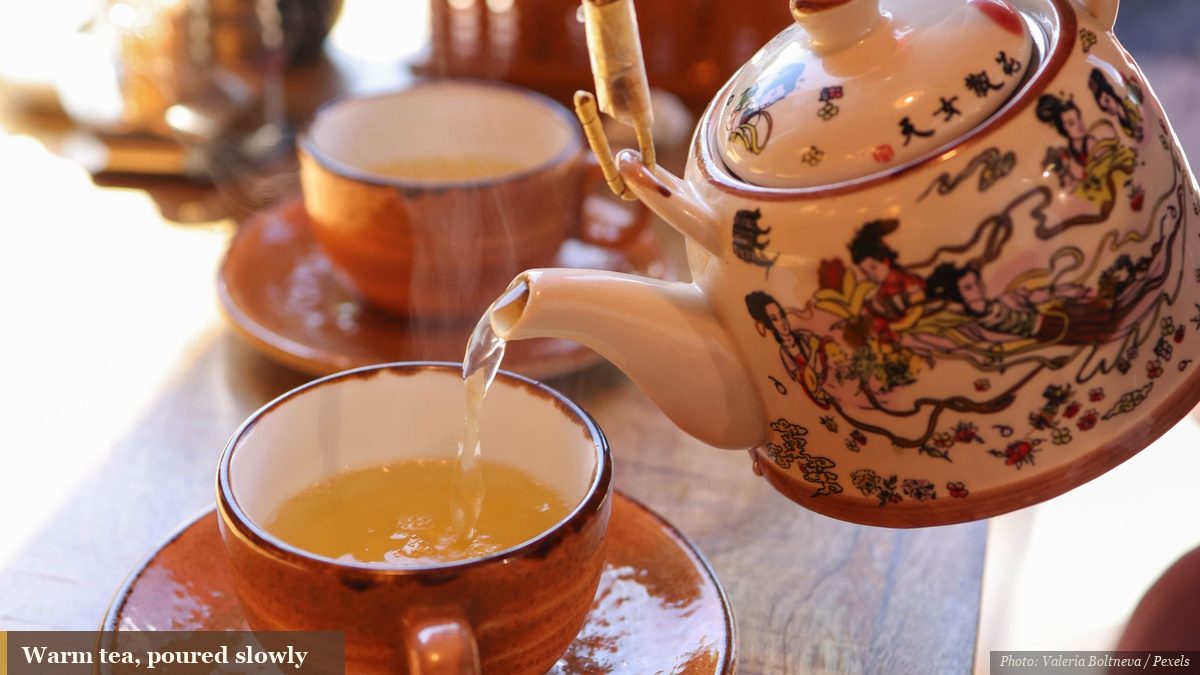 Warm tea poured from a painted ceramic Asian teapot into a small cup