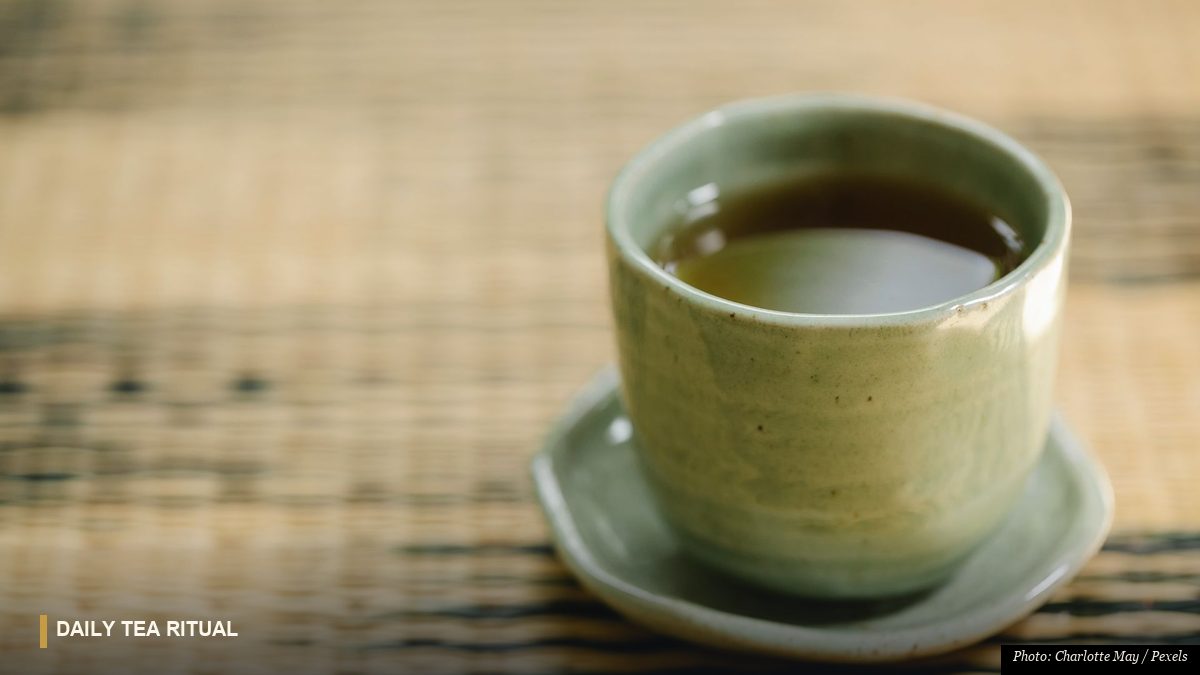 Celadon tea cup filled with warm herbal infusion resting on a bamboo mat