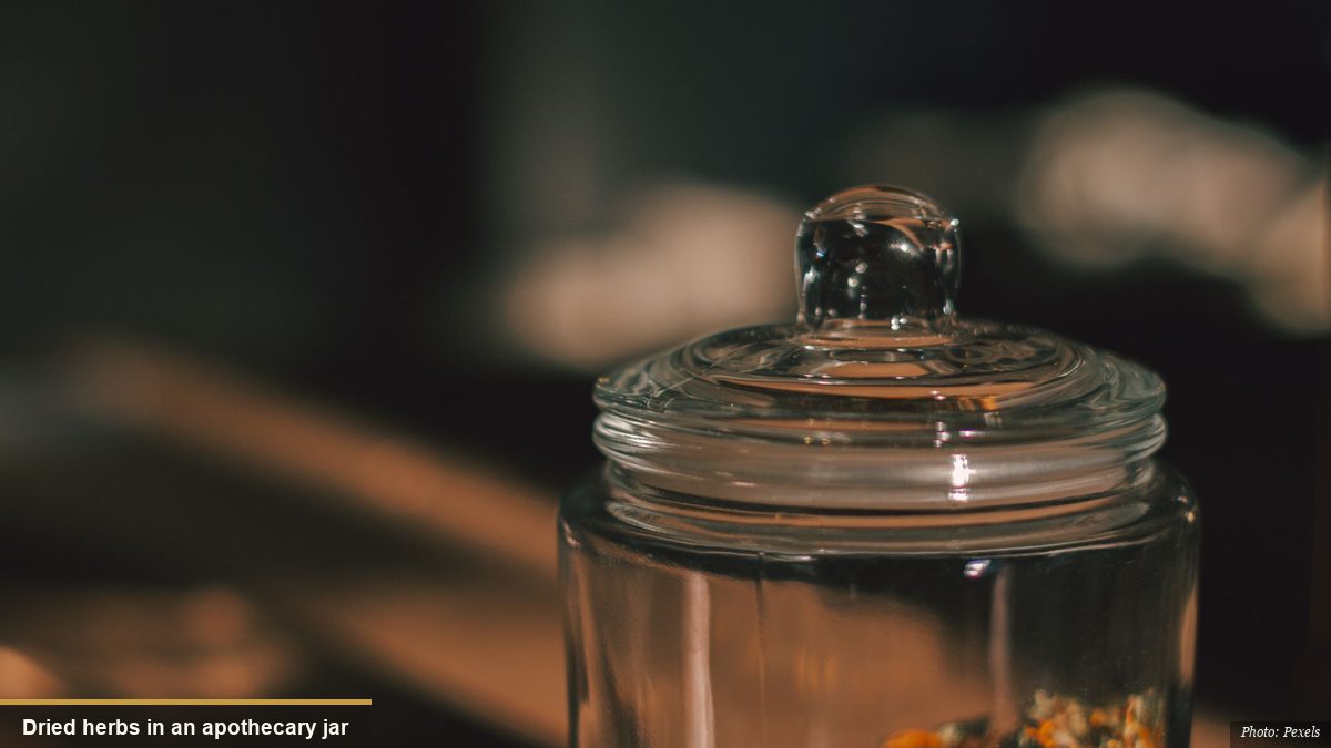 Glass jar of dried medicinal herbs and flowers on a wooden apothecary table
