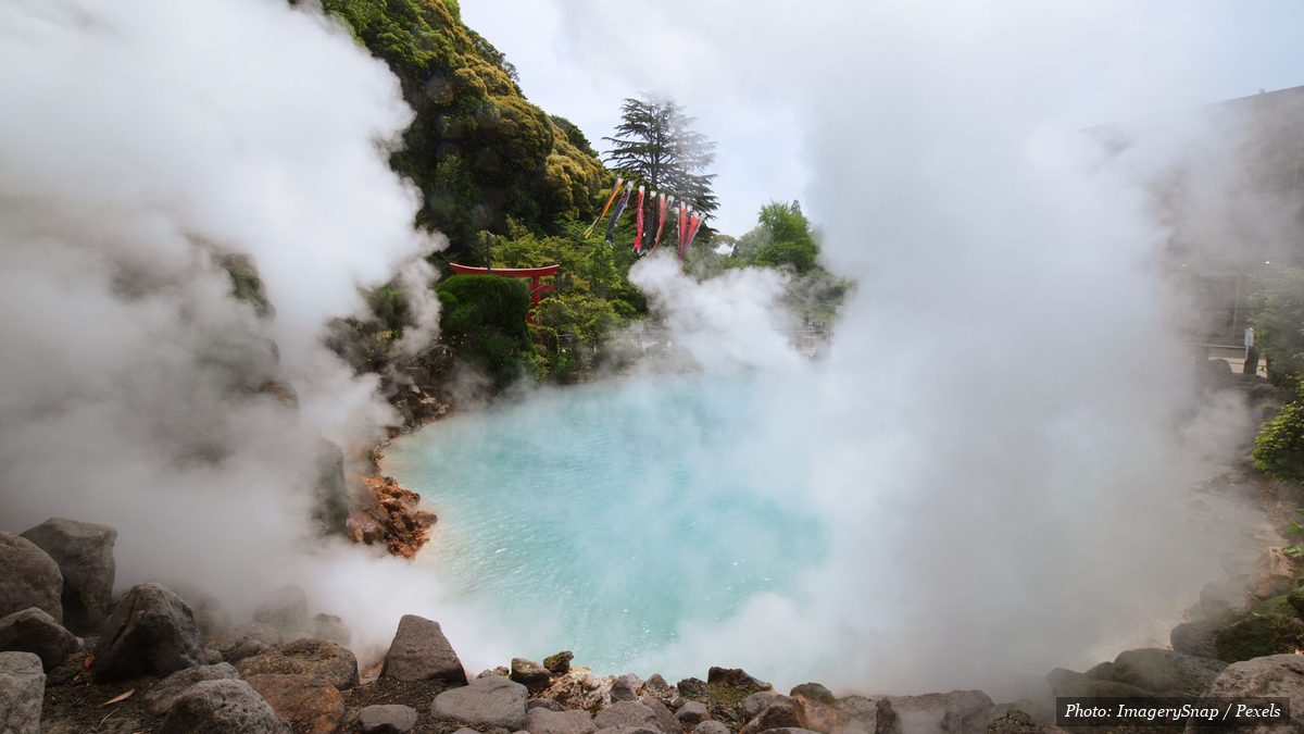 Steaming turquoise hot spring pool surrounded by rocks and greenery in Beppu Japan