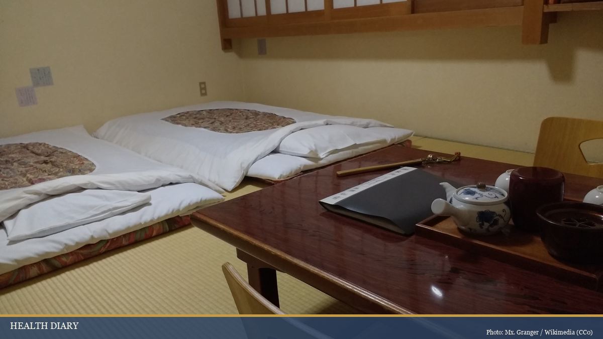 Traditional Japanese ryokan bedroom with white futon bedding laid on tatami mats and a low wooden tea table