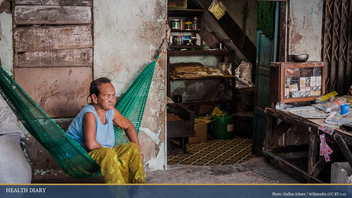 Vietnamese woman resting on a green mesh hammock outside a traditional house during midday siesta in Quy Nhon