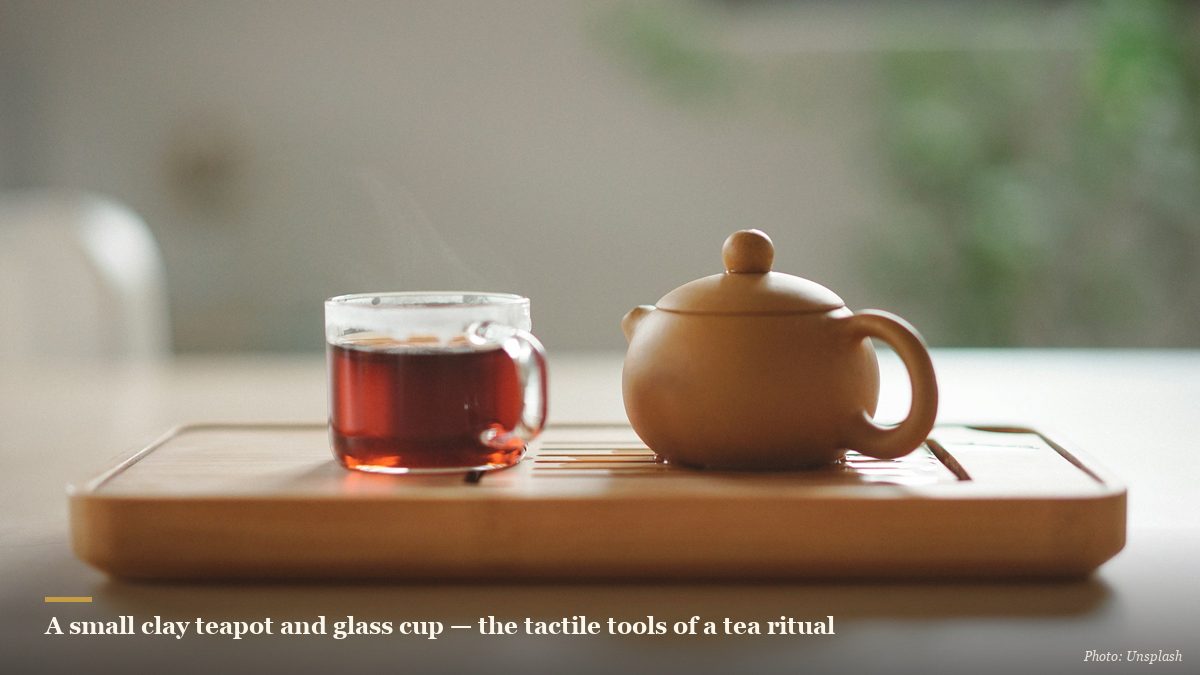 Small clay zisha teapot and glass cup of tea on a bamboo tray